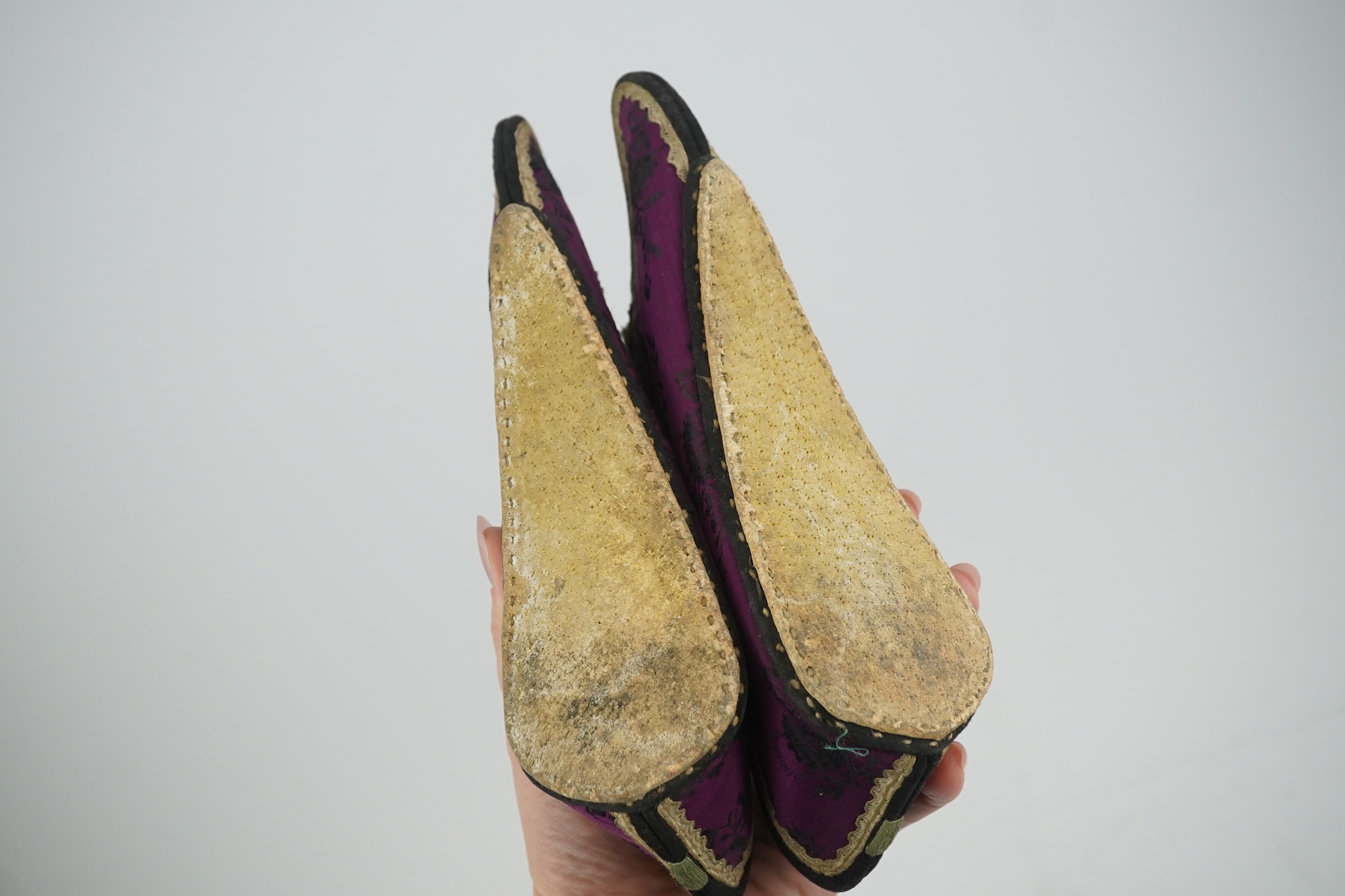 Four pairs of late 19th / early 20th Chinese ladies bound foot shoes, made in various coloured silks, with colourful floral embroidered motifs, two pairs with decorative silk pom-poms and another made of purple and black